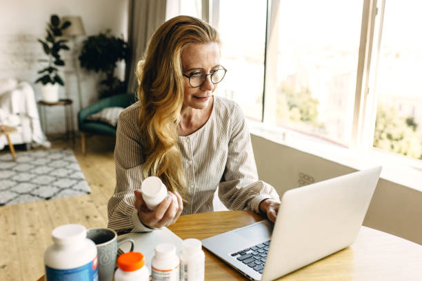 bem-humorada, blogueira envelhecida com longos cabelos dourados usando óculos que escrevem comentários online sobre novos suplementos alimentares para rejuvenescimento em sua conta via rede social, usando laptop - long red hair - fotografias e filmes do acervo