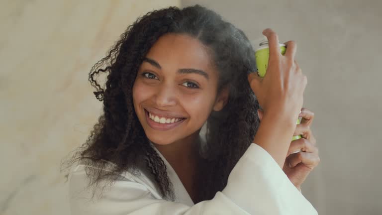 Hair Care cosmetics. Young african american woman spraying special conditioner on curly care, making hairstyle at home