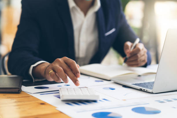 istock Businessman holding pen and pointing paper chart summary analyzing annual business report with using laptop at room office desk. 1371052792