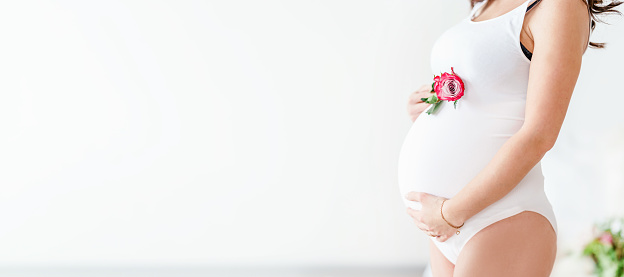 A pregnant woman in white clothes holds beautiful flowers. Cute concept healthy pregnancy, Motherhood, Mother's Day Holiday concept. Banner with copy space.