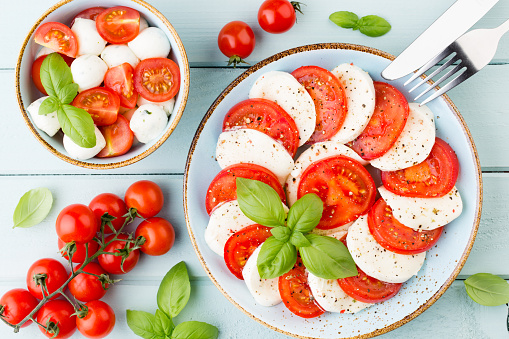 Tomatoes, mozzarella cheese, basil and spices on gray slate stone chalkboard. Italian traditional caprese salad ingredients. Mediterranean food.