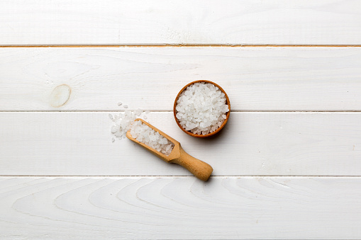 A wooden bowl of salt crystals on a wooden background. Salt in rustic bowls, top view with copy space.