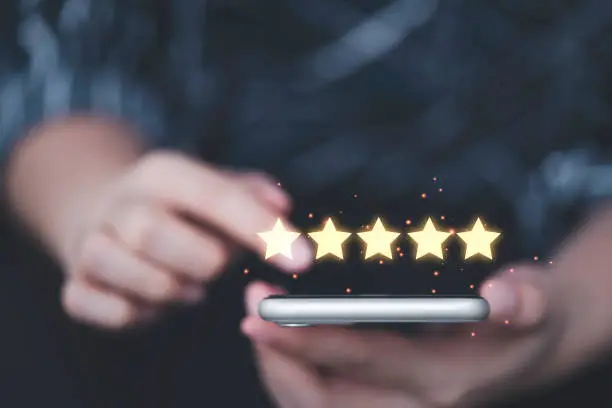 Photo of Businesswoman using smartphone  with yellow glowing five stars for client customer review product and service concept.