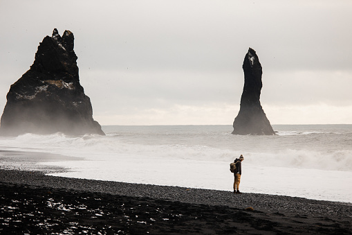 A young man standing and enjoy the view at Reynisfjara black sand beach with scenic view of Reynisdrangar on the background in winter in Iceland