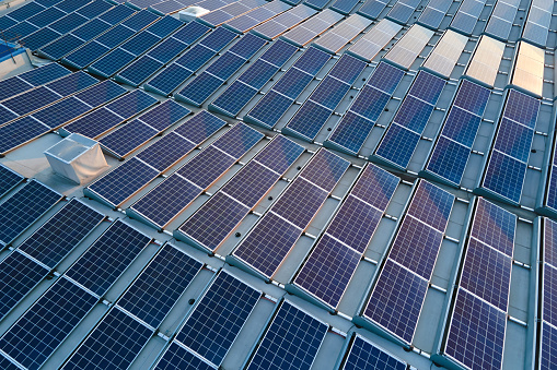 Aerial view of blue photovoltaic solar panels mounted on industrial building roof for producing green ecological electricity. Production of sustainable energy concept.