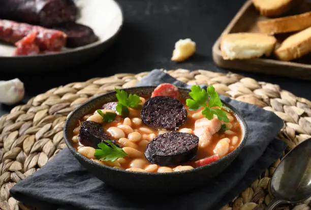 Photo of Spanish asturiana fabada with chorizo and morcilla on black background.