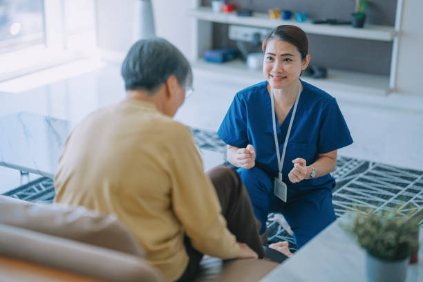 asiatisch-chinesische physiologin home caregiver ermutigt ältere frau, die mit ihren beinen beim radfahren trainiert - scrubs professional sport indoors healthcare and medicine stock-fotos und bilder