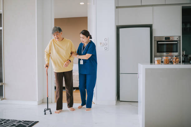 Asian Chinese female nurse helping senior woman practise walk with walking stick in living room. Senior patient with walking frame and nurse Asian Chinese female nurse helping senior woman practise walk with walking stick in living room. Senior patient with walking frame and nurse Dementia Patients stock pictures, royalty-free photos & images