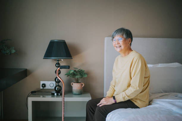 femme âgée chinoise asiatique souriant joyeusement assise sur le lit regardant ailleurs - using computer bedroom one woman only cheerful photos et images de collection