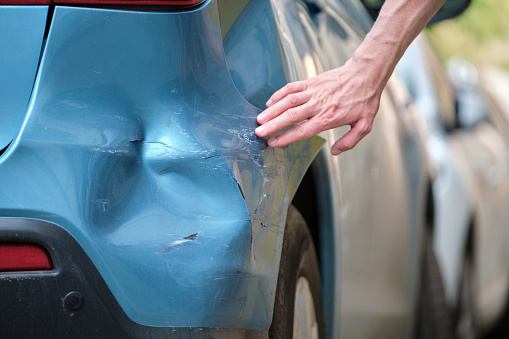 La mano del conductor examina el automóvil abollado con el guardabarros dañado estacionado en el lado de la calle de la ciudad. Concepto de seguridad vial y seguro de vehículos photo