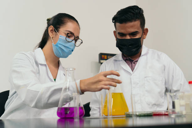 istock Two scientists working in the lab, The man holds a glass ball while his colleague analyzes it. Wearing protective masks as the new normal during the COVID-19 pandemic. 1371064456