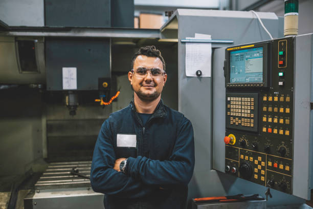 Portrait of smiling male apprentice engineer working with CNC machine in factory stock photo