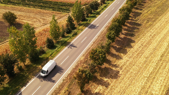 Minivan on the road, aerial view. Drone photography of white van vehicle driving through countryside landscape in summer.