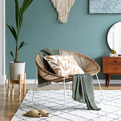 Elegante composición de creativo y acogedor interior de sala de estar con mesa de centro, sillón de ratán, plantas, alfombra y hermosos accesorios boho. Paredes de eucalipto y suelo de parquet. photo
