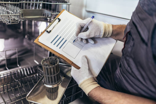 Male Technician Sitting Near Dishwasher Writing On Clipboard In Kitchen stock photo
