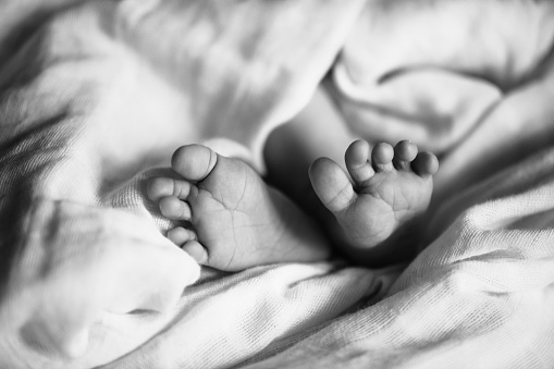 Tiny feet of newborn. Soft feet of baby on white blanket at home. Selective focus.