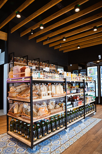 Fresh bread packages along with drinks arranged in rack. Food merchandise is on display at convenience store. Interior of illuminated delicatessen.