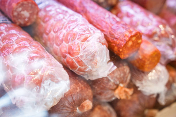 Fresh sausages in plastic packages at convenience store. Red raw meat on display at delicatessen. Close-up of merchandise.