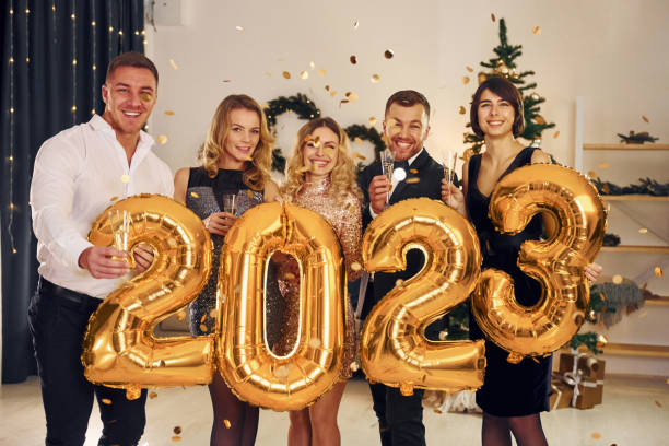 Holding balloons with 2023 number. Group of people have a new year party indoors together stock photo