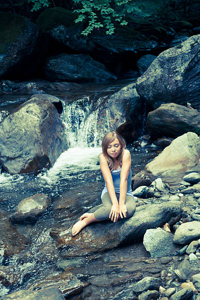 giovane ragazza seduta in una cascata. - waterfall zen like women meditating foto e immagini stock