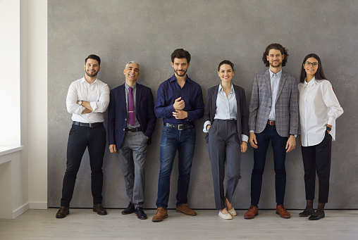 People who embody success and leadership. Group portrait of happy multi aged business professionals after meeting. Team of successful company employees or executives standing together near office wall