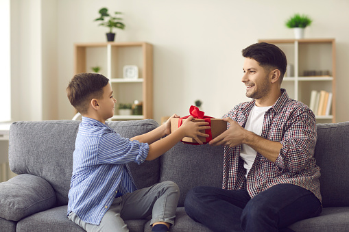 Surprise for dad and happiness moment. Cute boy gives congratulations to his dad on the holiday and gives him a gift box. Concept of men's day, father's day or birthday.