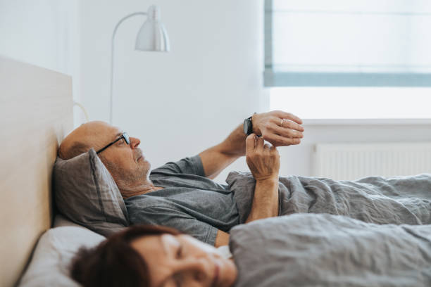 Senior man looking at smartwatch in bed Senior man analyzing his sleeping data from smartwatch. tracker stock pictures, royalty-free photos & images