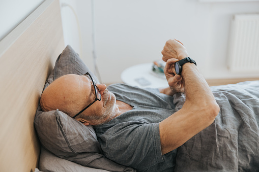 Senior man in bed, looking at sleeping data on his smartwatch.