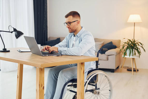 istock Working by using laptop. Disabled man in wheelchair is at home 1371088235