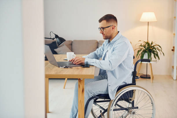 istock Working by using laptop. Disabled man in wheelchair is at home 1371088249