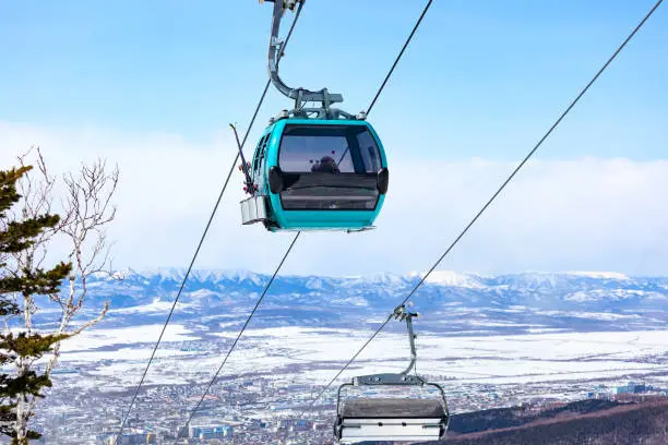 Cable car cabin with the skiers and snowboarders against the snow covered mountains and city
