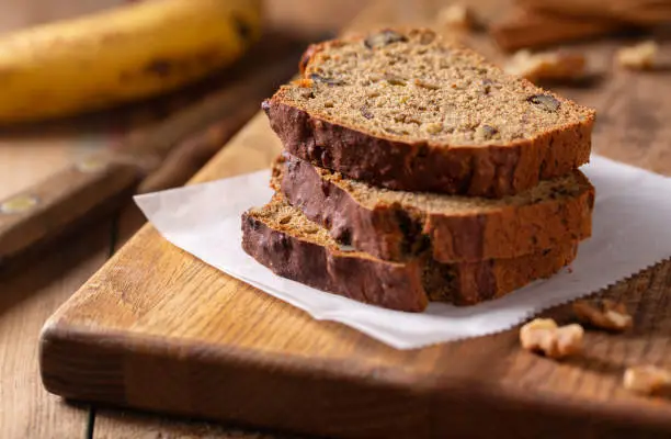 Slices of fresh baked banana nut bread with walnuts on rustic wood cutting board.