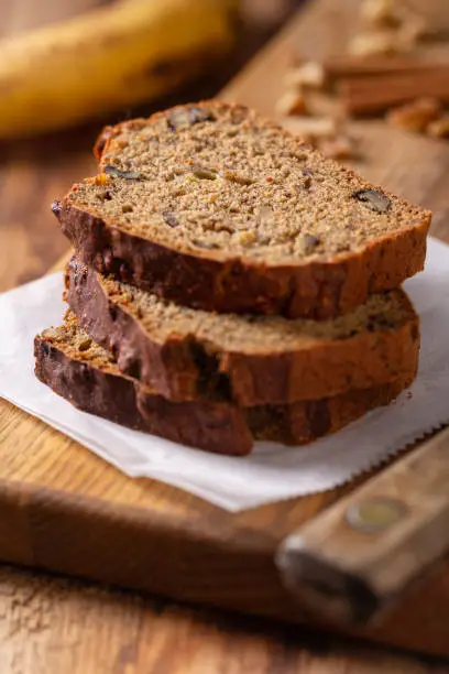 Slices of fresh baked banana nut bread with walnuts on rustic wood cutting board.