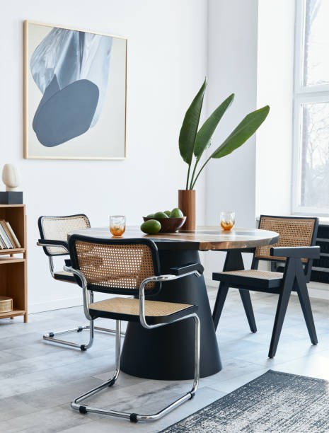 istock Stylish composition of dining room interior with design table, modern chairs, decoration, tropical leaf in vase, fruits, bookcase, abstract mock up paintings and elegant accessories in home decor. 1371092375