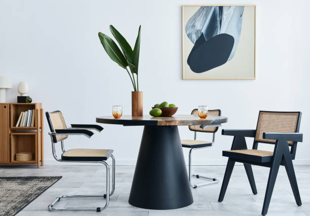 istock Stylish composition of dining room interior with design table, modern chairs, decoration, tropical leaf in vase, fruits, bookcase, abstract mock up paintings and elegant accessories in home decor. 1371092393