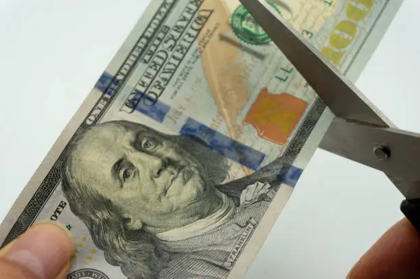 Photo of Scissors ready to cut a $100 US bill. Save money concept.Cutting costs.Financial themes.US$100 US Dollars.Economic crisis, deflation.Financial constraints.Cut budget inputs.Discounted products.