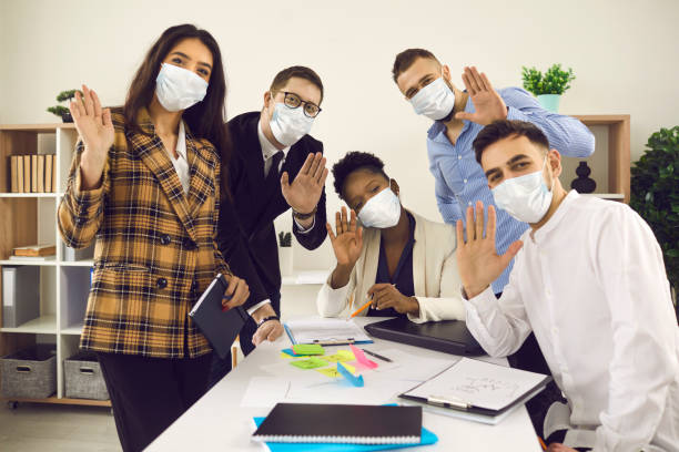 istock Happy creative office worker team in face mask waving hello to camera portrait 1371094974