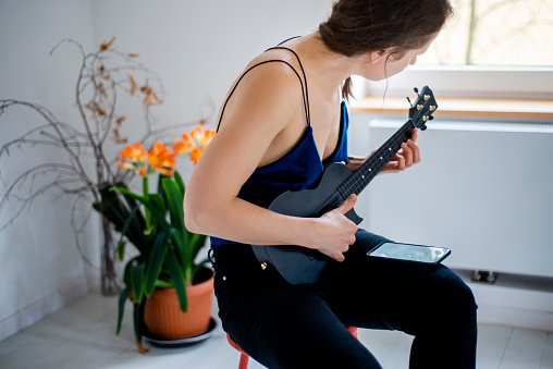 Woman in her late 30's learning to play ukulele with a mobile app.