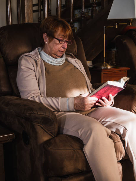 istock Old woman reading a book in a sofa 1371100011