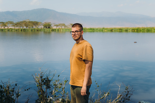 One man explorer enjoying safari trip staying at the lakeshore with a view of hippo floating in the water with mountain view