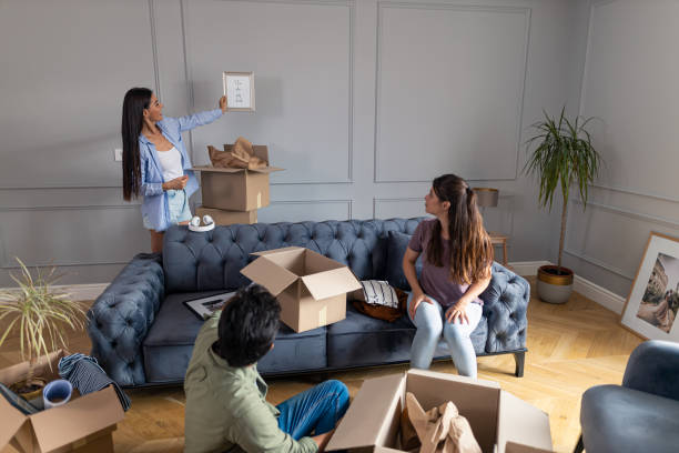 Smiling girl showing her friends how she will decorate their new apartment. Smiling girl took a picture from a cardboard box and leaned against the wall to show her friends how to decorate the space in the new apartment. roommate stock pictures, royalty-free photos & images