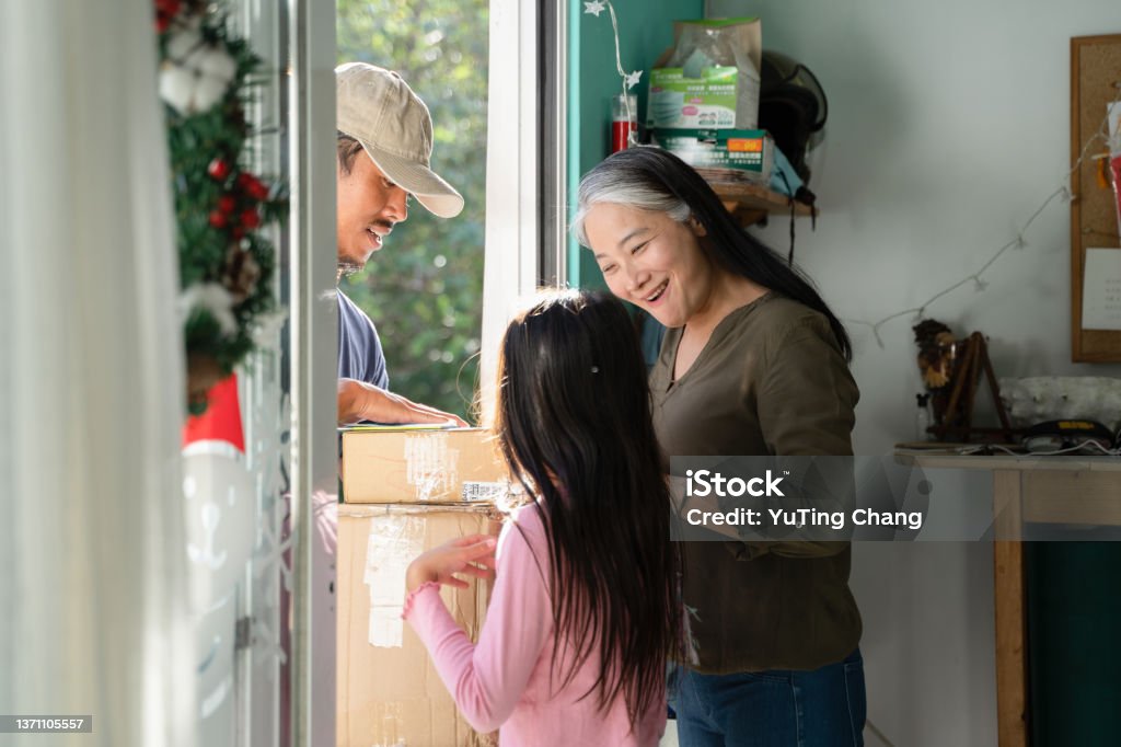 Mother and daughter received courier packages at Christmas Mother and daughter check delivery with happy courier at the front door, Delivery man handing over cardboard box to female customer, Christmas time, Christmas delivery, online shopping Box - Container Stock Photo