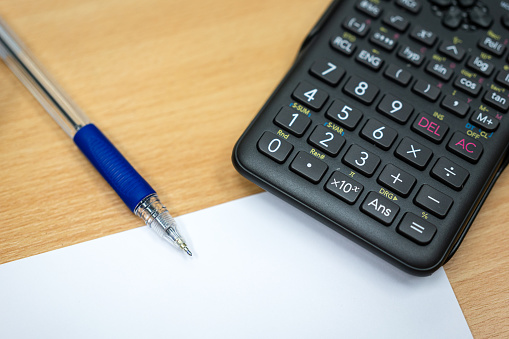 A digital calculator with ball pen and empty paper on the wooden table. Accounting finance job or education examination scene concept photo. Selective focus at calculator button.