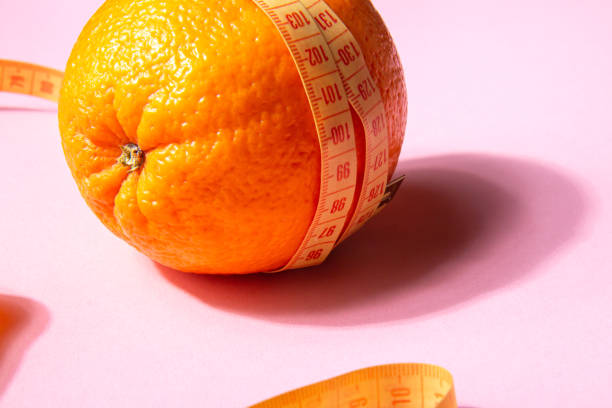 Bright yellow measuring tape wrapped around an orange on a pink background Bright yellow measuring tape wrapped around an orange isolated on a pink background. Close up cellulite stock pictures, royalty-free photos & images