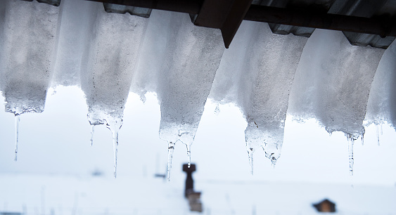 Ice and snow covers roof building, dangerous ice dams hanging from roof.  Danger and safety concept. Selective focus
