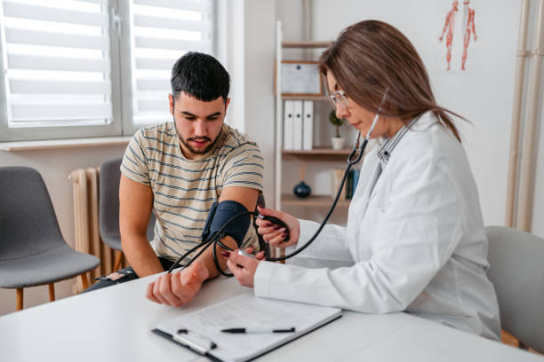 врач измеряет артериальное давление молодого пациента - doctors office stethoscope patient medical record стоковые фото и изображения