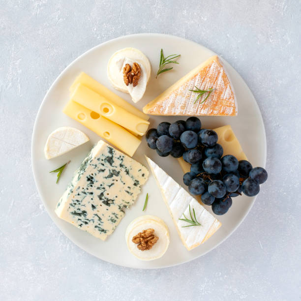 Cheese plate served with grapes and walnuts on a grey concrete background