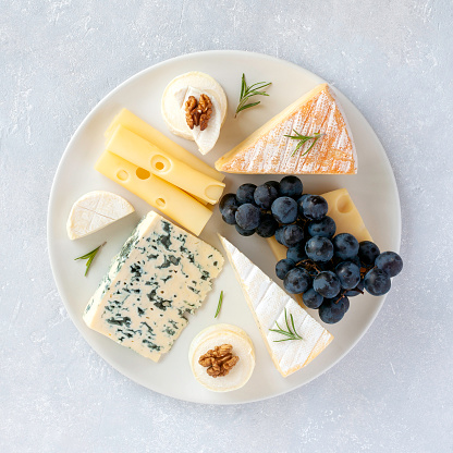 cheese plate served with grapes and walnuts on a grey concrete background, top view