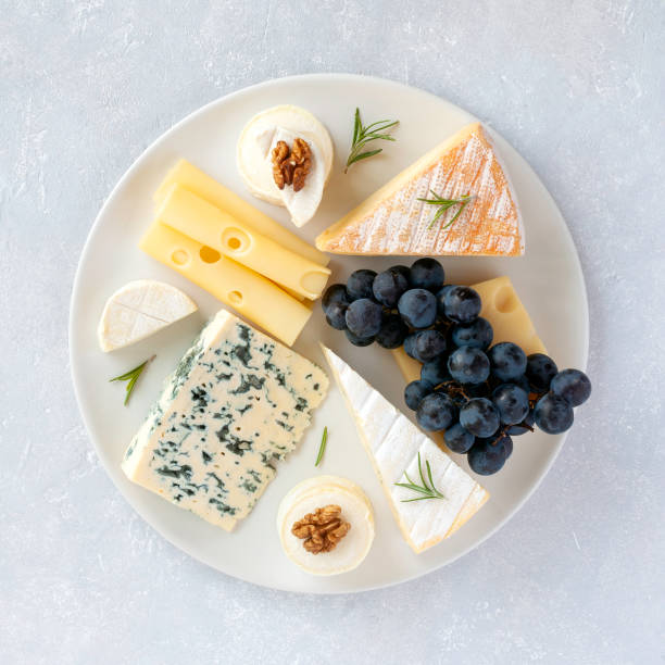 cheese plate served with grapes and walnuts on a grey concrete background - blue plate fotos imagens e fotografias de stock
