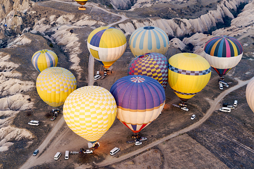 Balloons burning fuel as they fly over the city of Goreme in Cappadocia, with sightseeing tourists during a sunny summer day